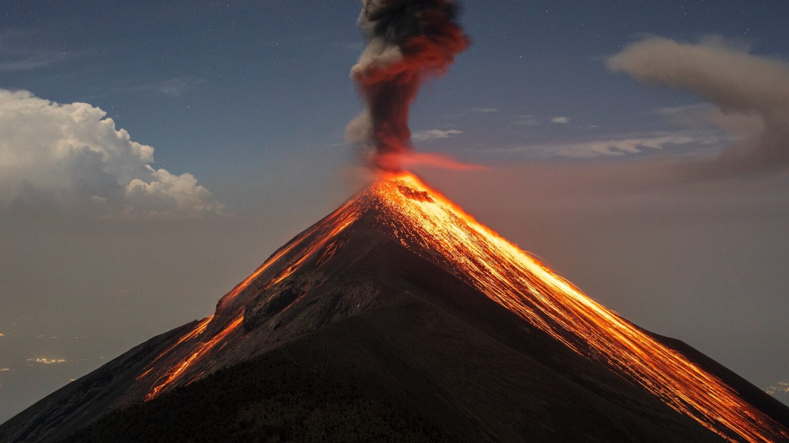 The volcano Fuego (Volcán de Fuego) erupting, spewing red-hot lava and billowing black smoke.