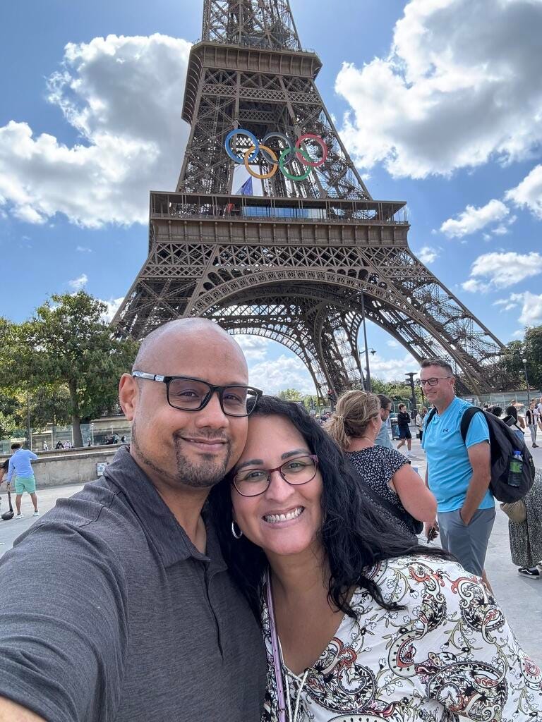 man and woman taking selfie in front of eiffel tower with olympic rings on it