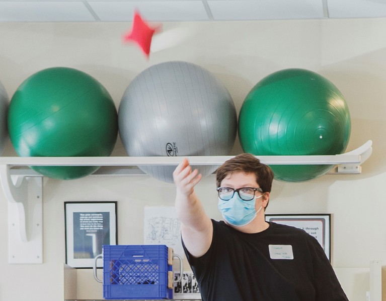 A young man throws a beanbag high into the air in a gym setting