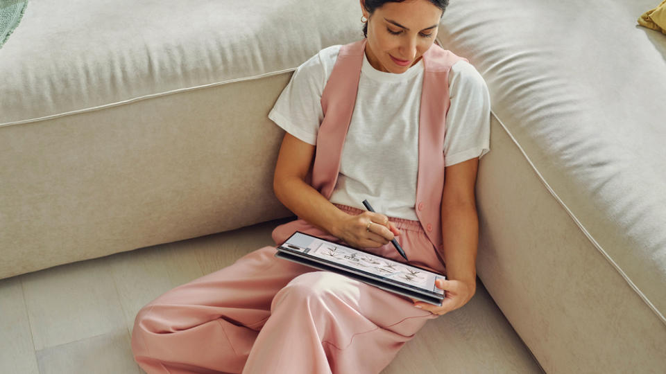 A person sitting on a couch, sketching with a stylus on the HP OmniBook Ultra Flip 14-inch.