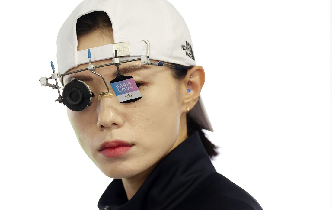 Kim Yeji wears her shooting glasses and a white baseball cap facing backwards.