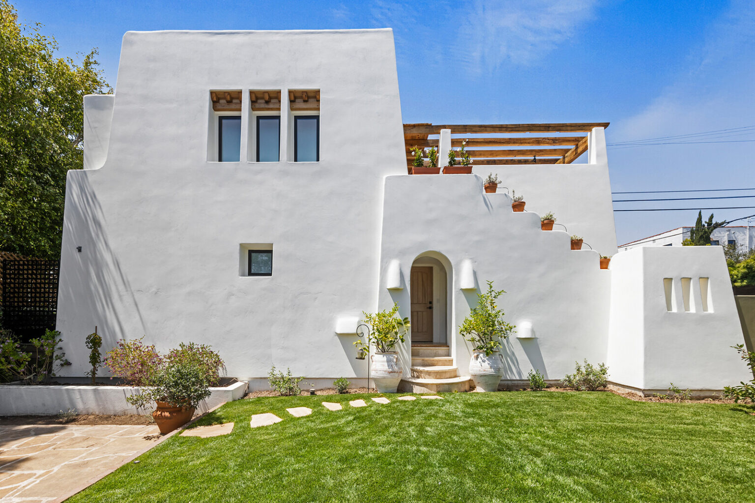 The newly built home has a crisp, white exterior and a sun-kissed living area that opens to a pergola-topped balcony.