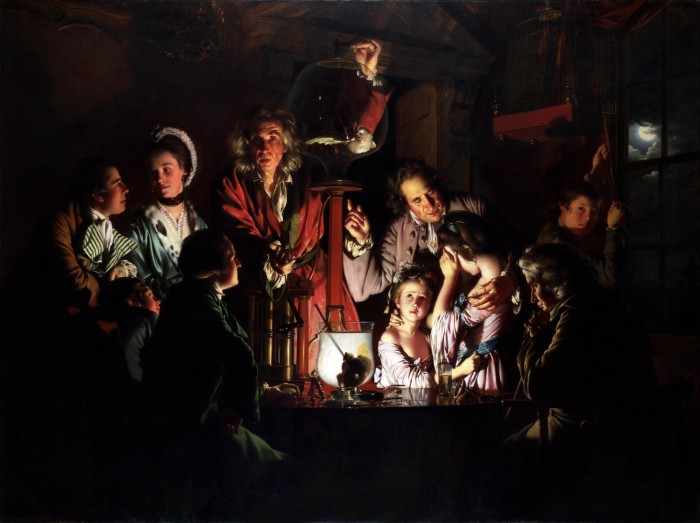 A group of people in 18th-century dress gather around a table in a dark room, the only light coming from a candle glowing behind a glass bowl. A man holds up a glass jar containing a small bird. Some of the audience watch in fascination, others look horrified. One young girl covers her eyes