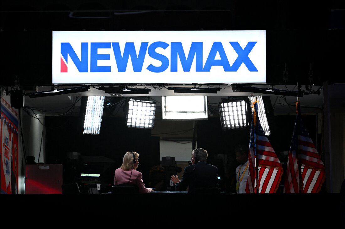 News anchors work at Newsmax's booth during the 2024 Republican National Convention in Milwaukee, Wisconsin. The network has settled with voting-tech company Smartmatic on the eve of trial.