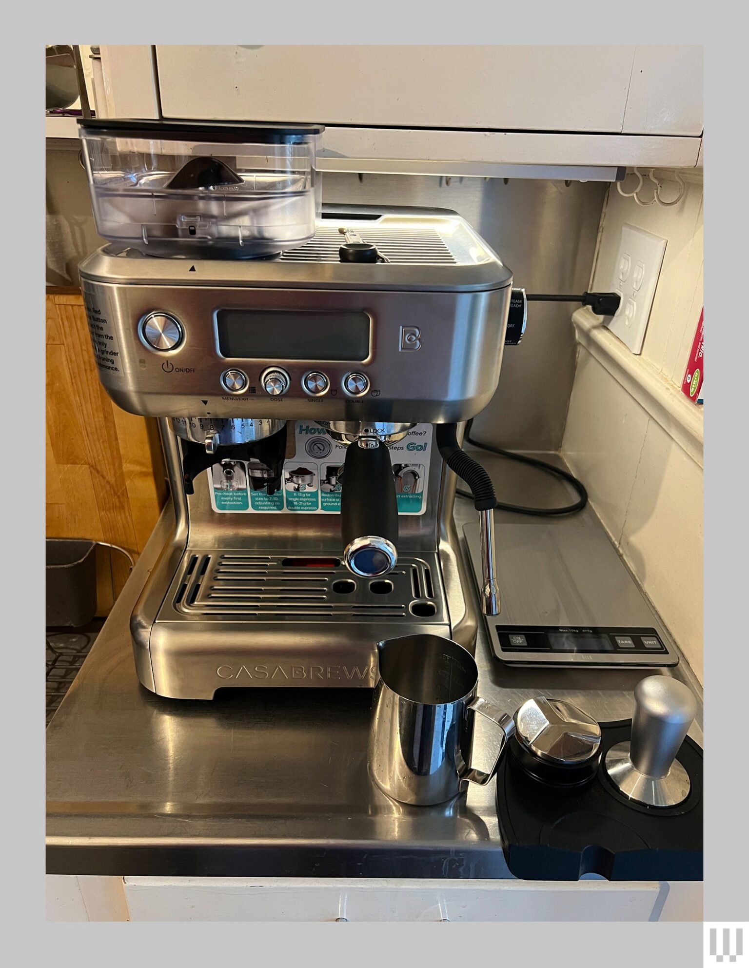 Front view of Casabrews 5700 Pro a silver espresso machine with a small digital screen sitting on a metallic surface...