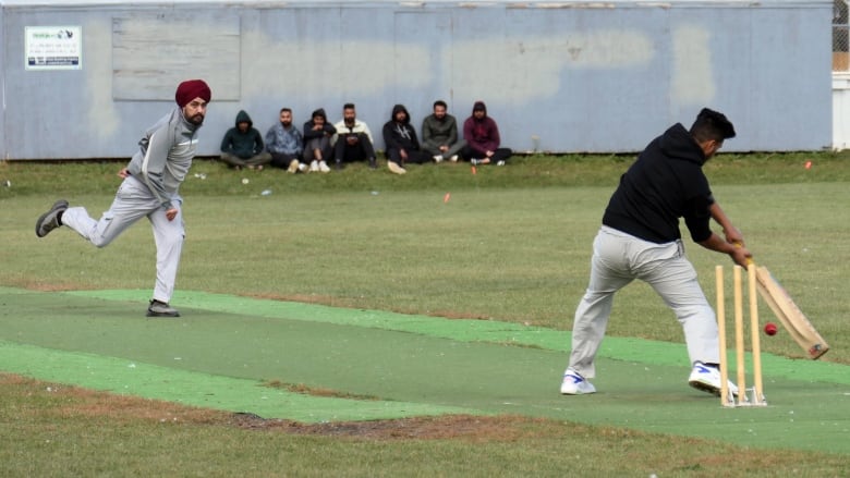 A cricket bowler looks a batter who is about to hit the ball.