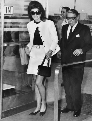 Wearing mod sunglasses and a miniskirt, Jacqueline Kennedy Onassis accompanies her husband, Aristotle, to a plane at Kennedy Airport on today, before the Greek shipping magnate took off for Athens. Ari was flying his own Olympic Airways to Europe and Jackie came along to the airport to say goodbye.