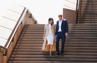 Meghan Markle wears a white dress and tan trench coat she descends the Sydney Opera House steps with Prince Harry