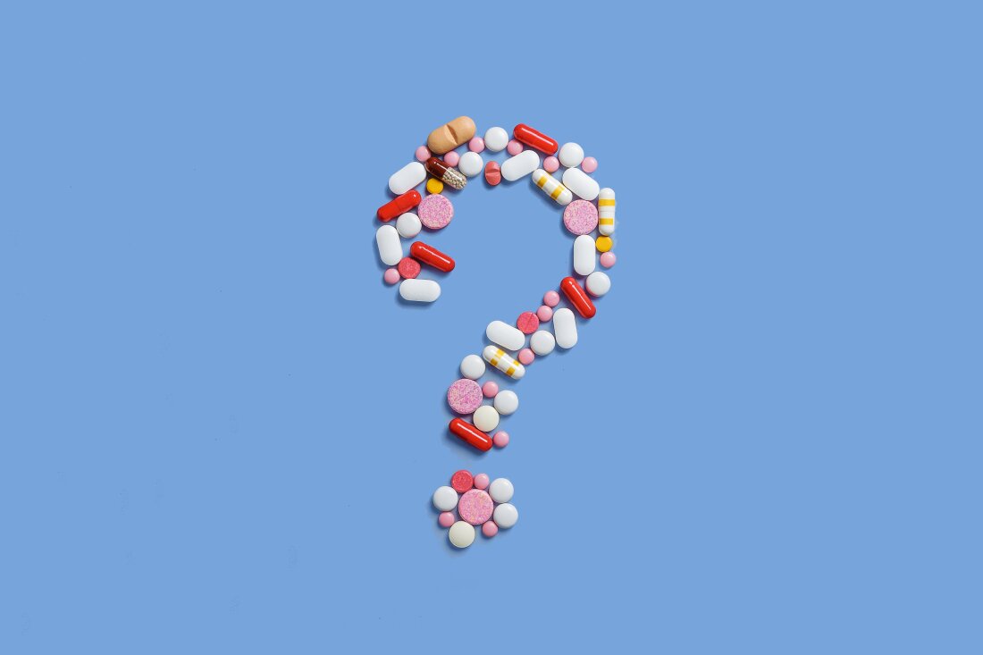 A lot of pills scattered on a blue background. A question mark laid out of pills. Counterfeit medicinal products. Empty space to insert text