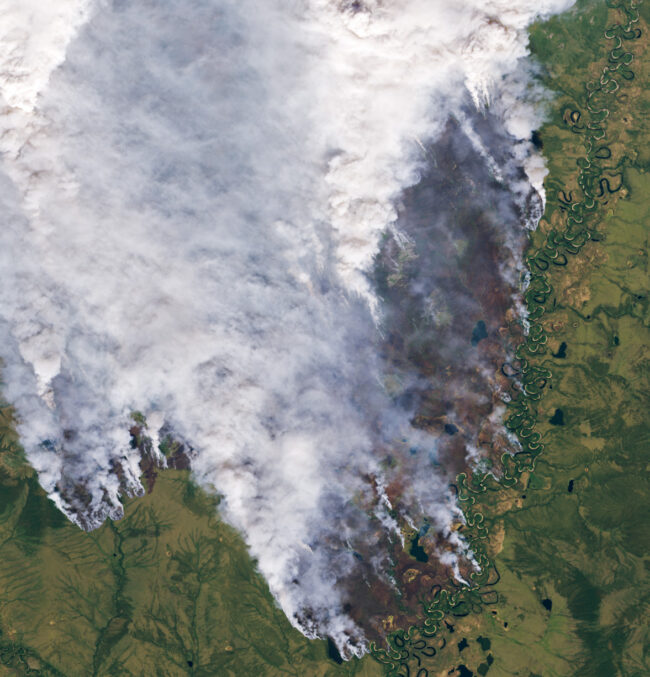 Satellite view of green and brown landscape and snaky river with smoke from forest fires covering most the image.