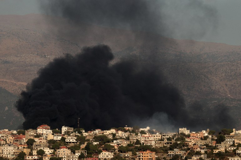 a large black cloud of smoke rises above a village