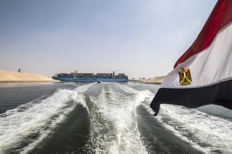 An Egyptian national flag flies on a boat as showsa container ship sails down at the new section of the Suez Canal in the Egyptian port city of Ismailia, 135 kms northeast of Cairo on October 14, 2019. - Since the Suez Canal was inaugurated amid pomp and ceremony 150 years ago, it has become one of the world's most important waterways. But its anniversary will only be discreetly marked in Egypt.