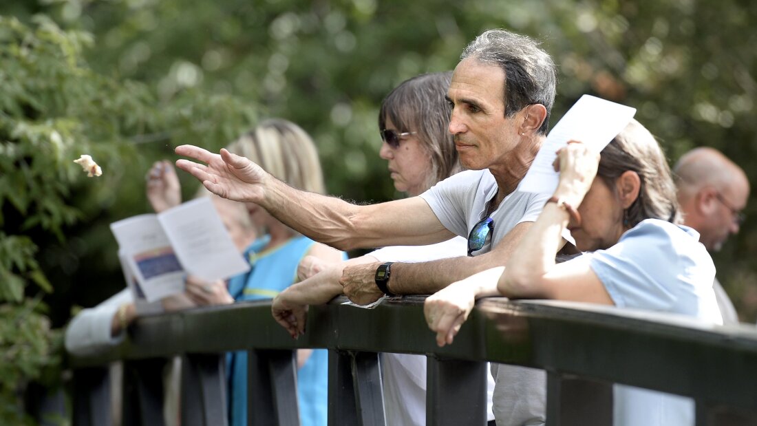 A man stands with others along a bridge as he throws a piece bread into a creek in Boulder, Colorado. This is part of a tashlich ceremony, which involves symbolically casting away sins.