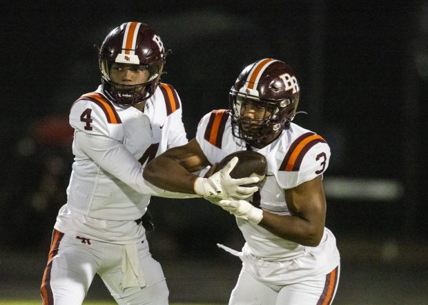 Brother Rice's CJ Gray (4) hands the ball off to Tyler Lofton (3) during a CCL/ESCC crossover game in Burbank on Friday, Oct. 18, 2024. (Vincent D. Johnson / for the Daily Southtown)