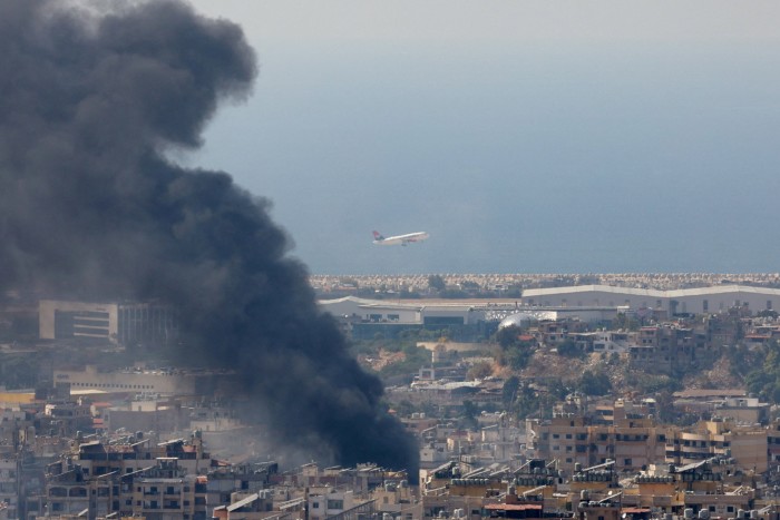 Smoke rises in Beirut’s southern suburbs after a strike, as a plane takes off from Rafic Hariri International Airport