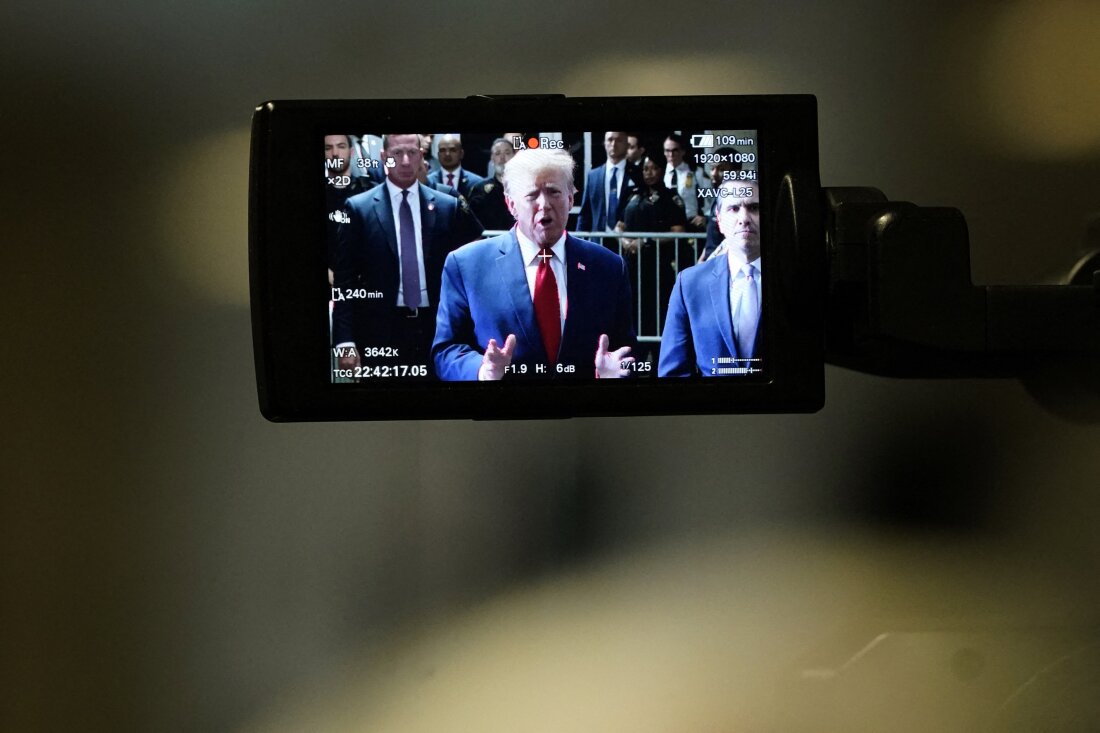 This photo shows former President Donald Trump on a camera monitor as he speaks to the press in February outside Manhattan Criminal Court. He's wearing a blue suit jacket, a red tie and a white shirt. Many people in suits and law enforcement uniforms stand behind him.