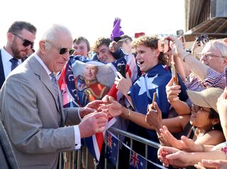 King Charles wears a gray suit and sunglasses to greet Australian fans waving flags outside the Sydney Opera House