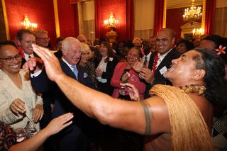 King Charles wearing a suit and dancing with a group of guests at Buckingham Palace