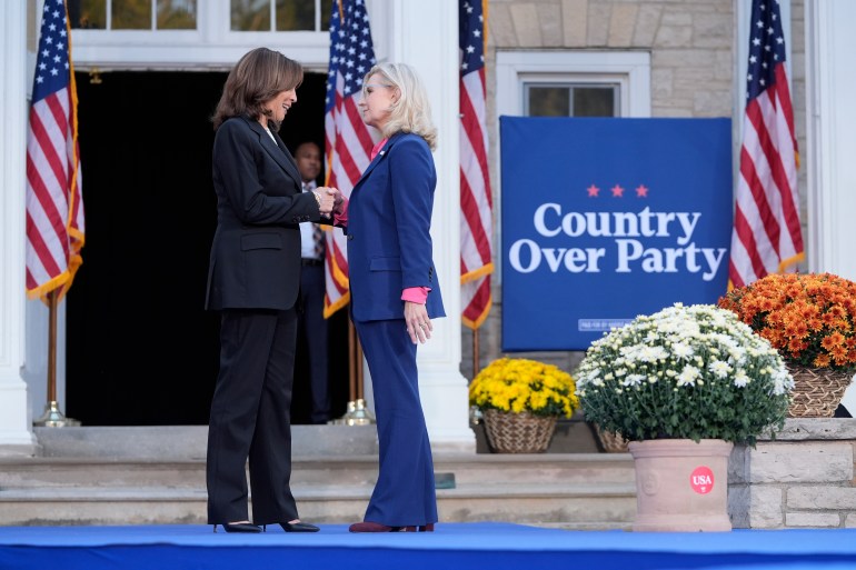 Kamala Harris and Liz Cheney shake hands on stage in front of a sign that reads: "Country over Party."