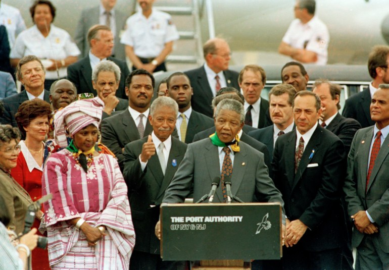 Nelson Mandela addresses the crowd at John F. Kennedy International Airport after arriving in New York, June 20, 1990. With Mandela from left are: wife of New York City Mayor David Dinkins, Joyce Dinkins; New York City Comptroller Liz Holtzman (red dress) Winnie Mandela, his wife, Jesse Jackson, Mayor Dinkins and New York Governor Mario Cuomo. Others are unidentified. (AP Photo/Charles Rex Arbogast)