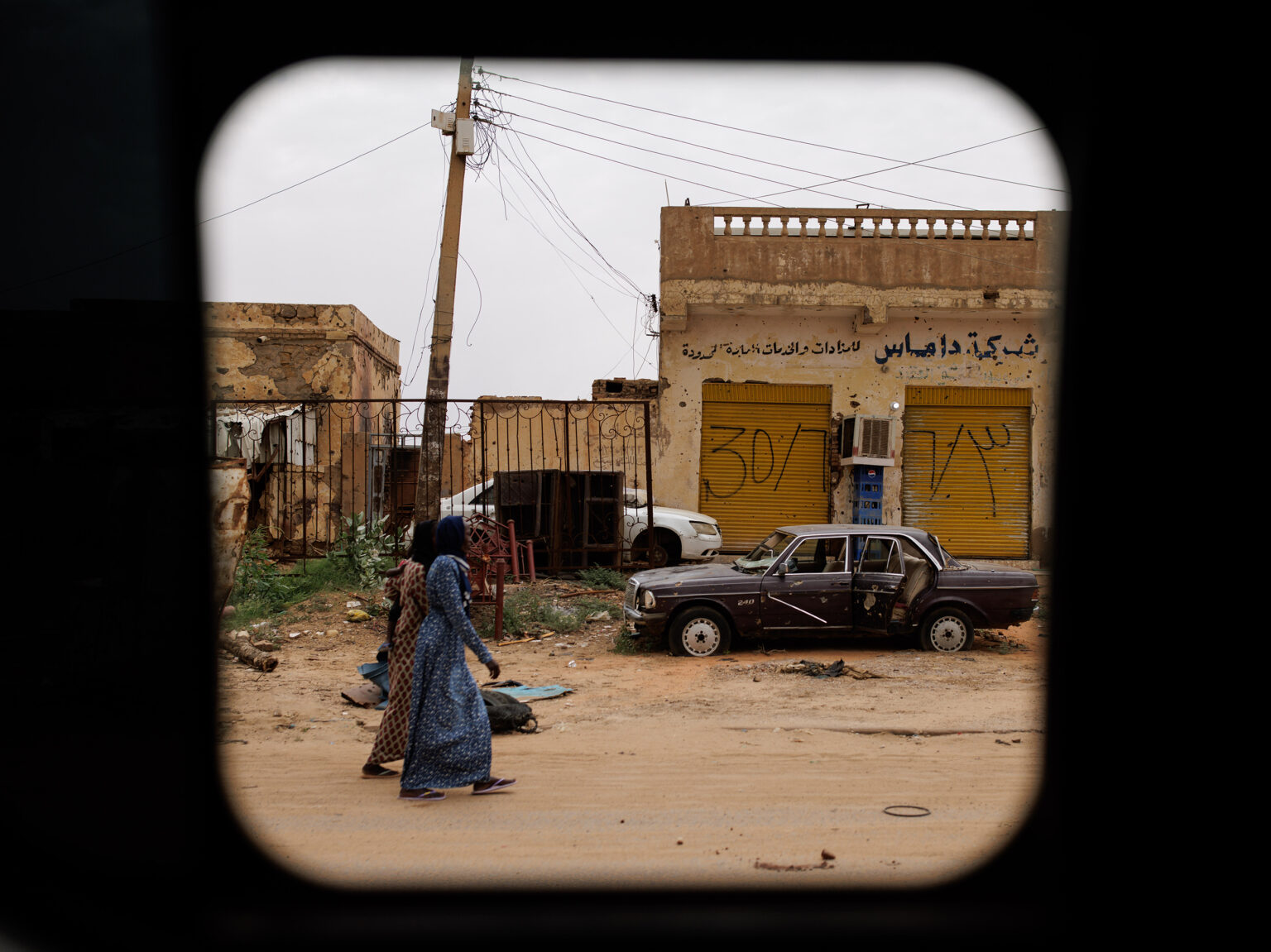 Two women walk past a car destroyed by fighting, as seen through a car window, in Omdurman, Republic of the Sudan on September 5.