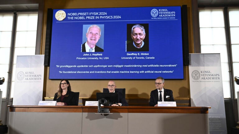 Photos of John Hopfield and Geoffrey Hinton appear on a screen as Hans Ellergren, center, permanent secretary at the Swedish Academy of Sciences in Stockholm, makes the award announcement.