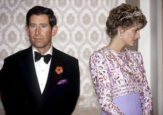 Prince Charles wearing a tuxedo and looking downcast standing next to Princess Diana who is turned away from him and wearing a purple dress and tiara