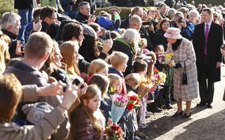 Queen Elizabeth in a pink coat meeting a crowd of people and taking a bouquet of flowers