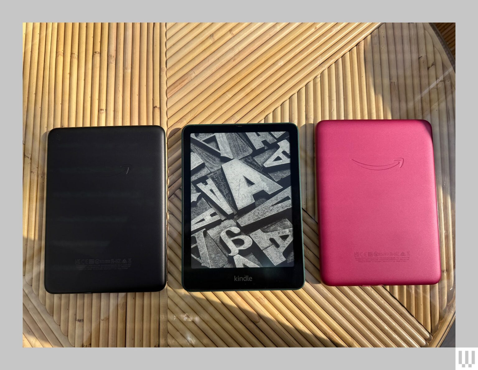 Front and back views of the Kindle Paperwhite three small ereaders in black blue and pink laying flat on a bamboo surface