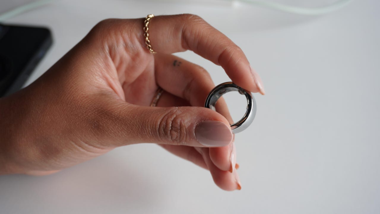 A hand is holding a silver Oura Ring