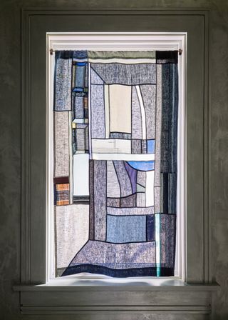 A blue and white patchwork Pojagi hanging in a window