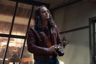 Daniel Zovatto as Rodney alcala holding a camera in a woman's apartment in the movie woman of the hour